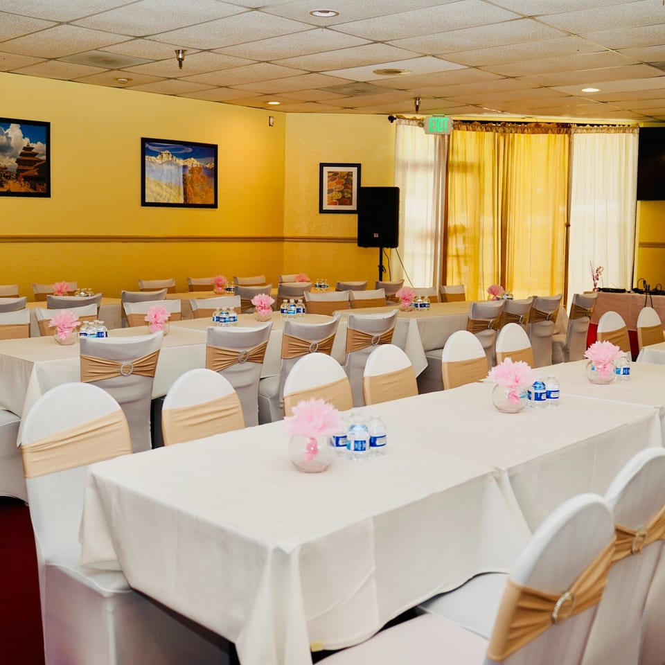 Tandoor Restaurant's dining room set up for an event with white tablecloths, chairs, and pink floral centerpieces.