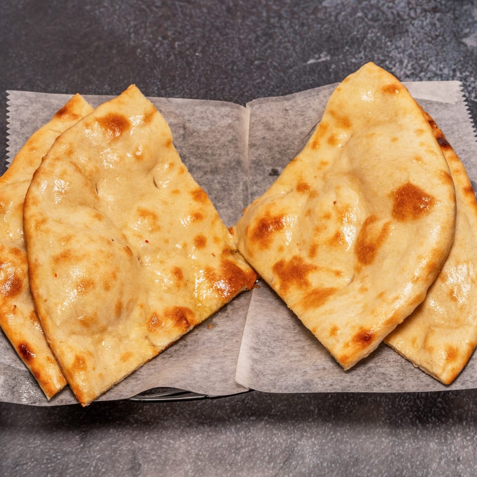Four pieces of golden-brown Indian naan bread, lightly oiled, served on white parchment paper.