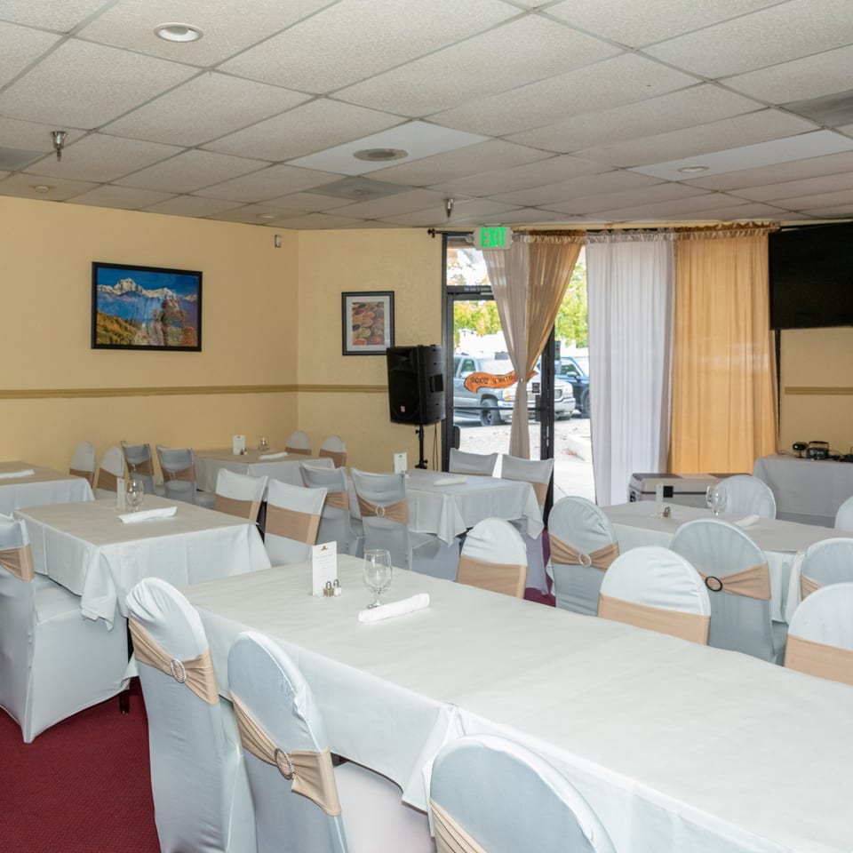 Empty dining room at Tandoor Restaurant with white tablecloths, chair covers, and beige sashes.