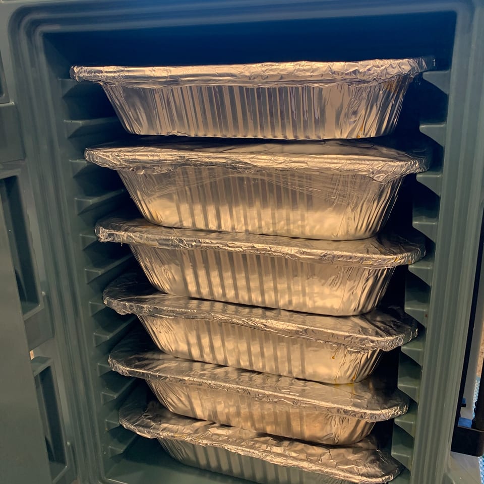 Stacked foil containers of Indian food, ready for catering or delivery, inside a warming unit.