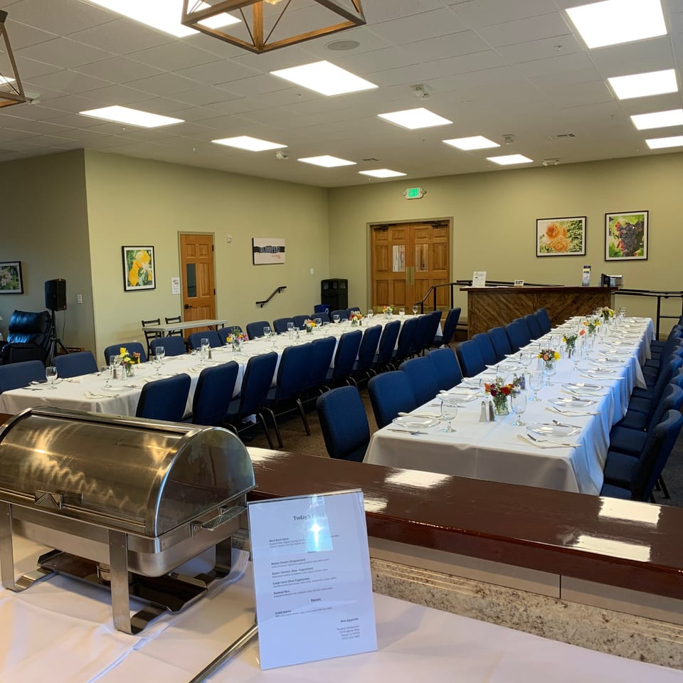 A large dining room at Tandoor Restaurant with long tables set for a banquet and a buffet warmer.
