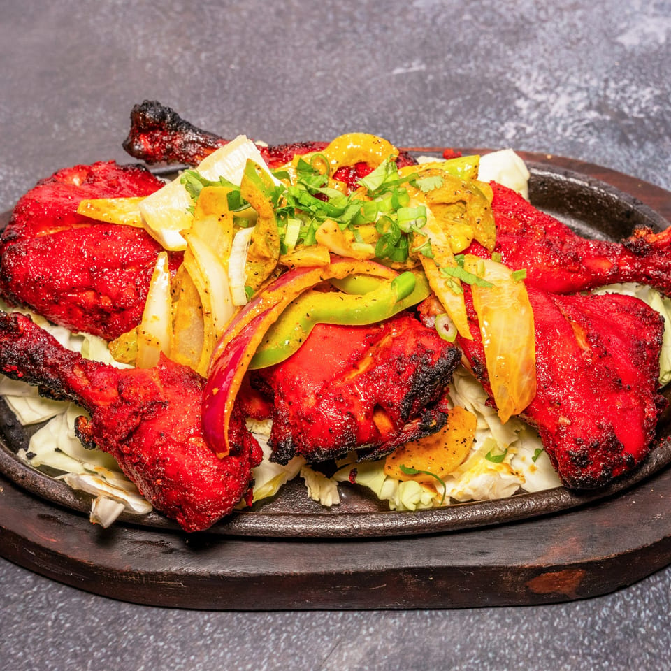 Tandoori chicken, bright red and charred, served on a sizzling platter with onions and peppers.