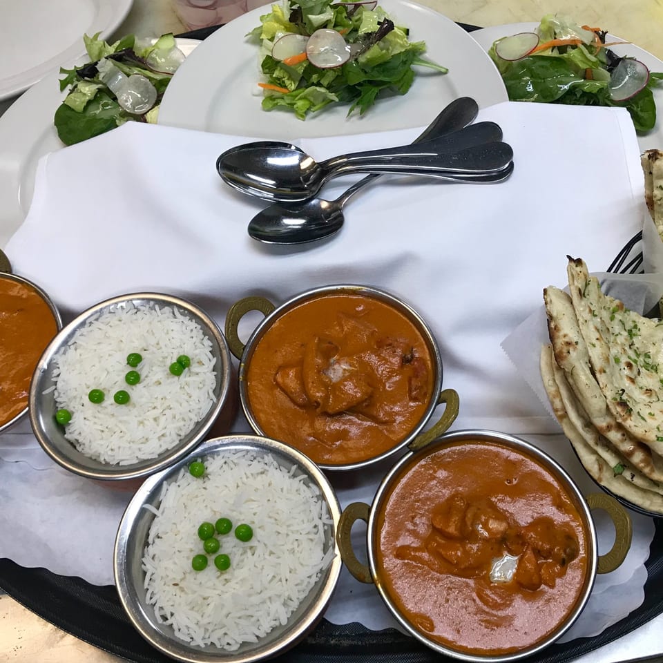 Indian meal with three bowls of butter chicken, three bowls of rice with peas, naan, and salads.