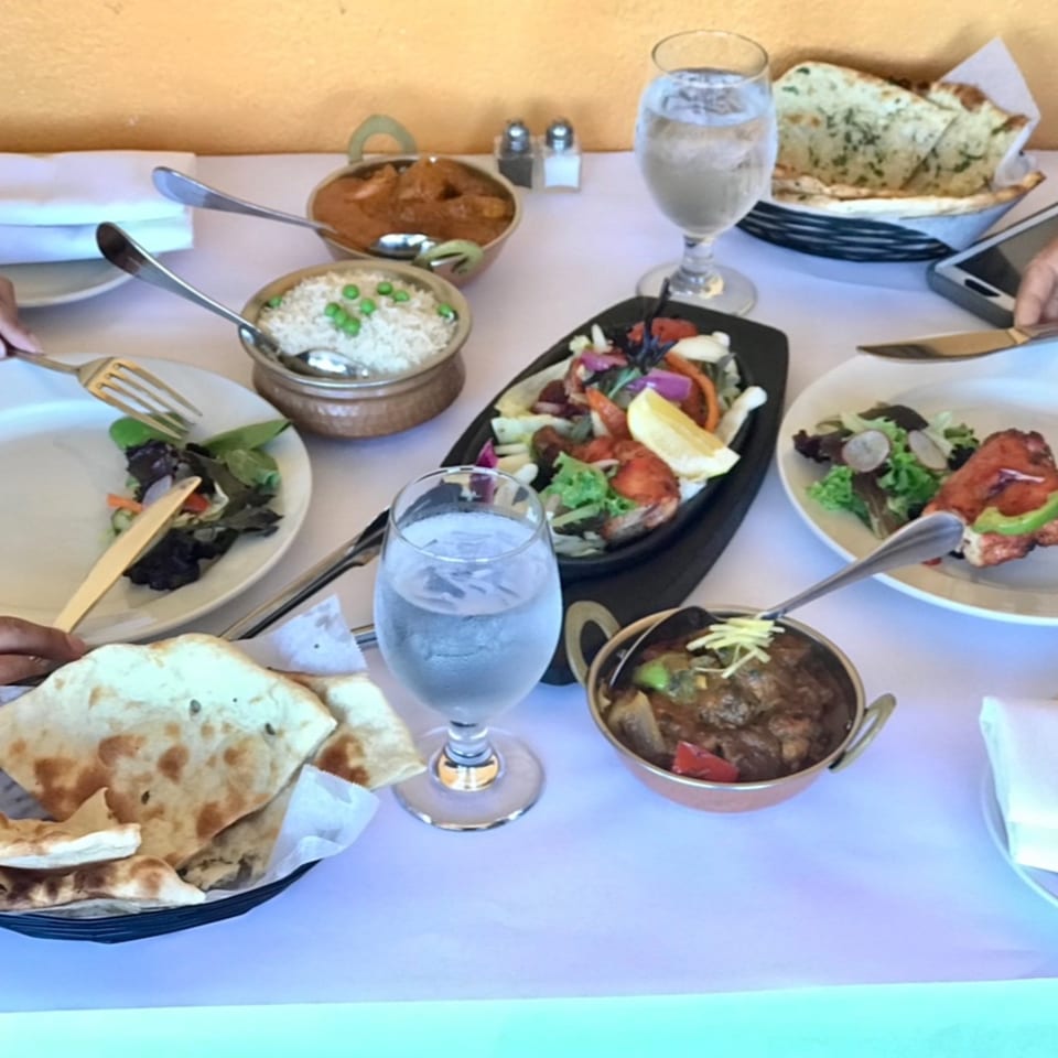 A table laden with various Indian dishes, including curries, rice, naan bread, and salads.