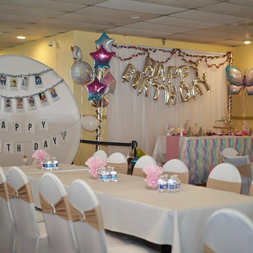A decorated room for a birthday party with balloons, banners, and tables set with chairs.