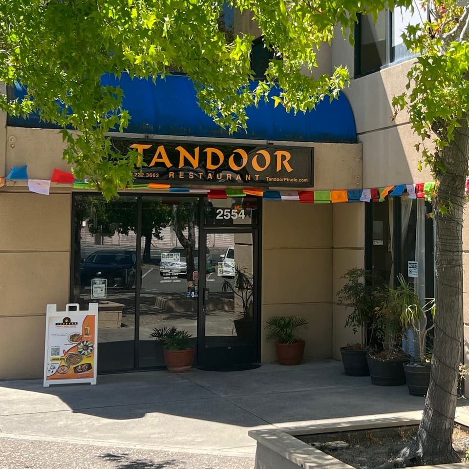 The exterior of Tandoor Restaurant, an Indian and Nepalese eatery, with a blue awning and prayer flags.