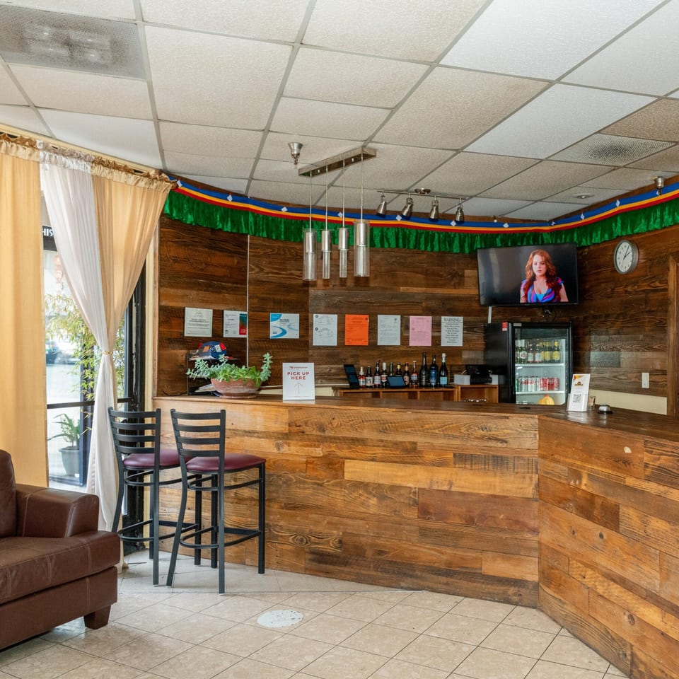 Tandoor Restaurant's interior features a wooden counter, bar stools, a TV, and a refrigerator with drinks.
