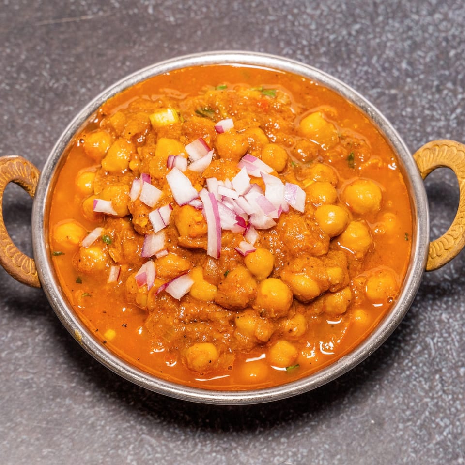 Tandoor Restaurant's Chana Masala, a chickpea curry topped with diced red onions in a metal bowl.