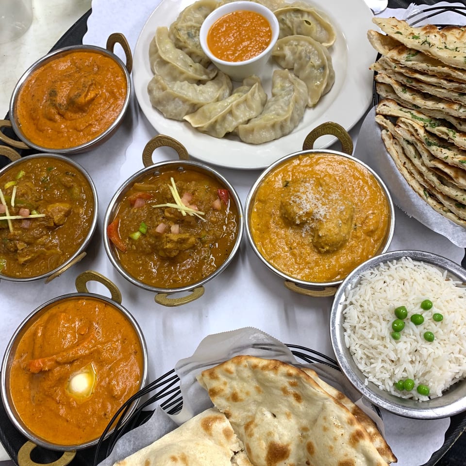 A feast of Indian dishes, including various curries, momos, naan bread, and rice with peas.