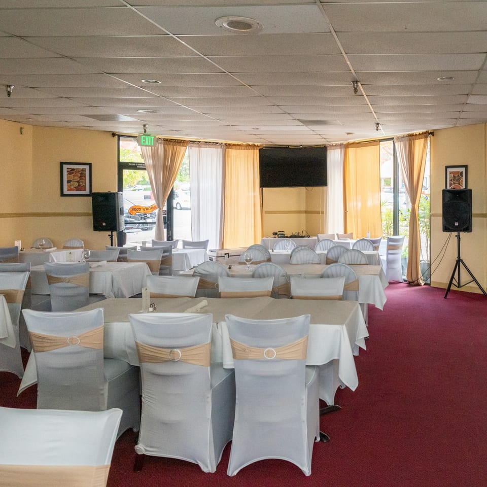 Empty dining room at Tandoor Restaurant with tables set for a banquet, featuring white and gold decor.