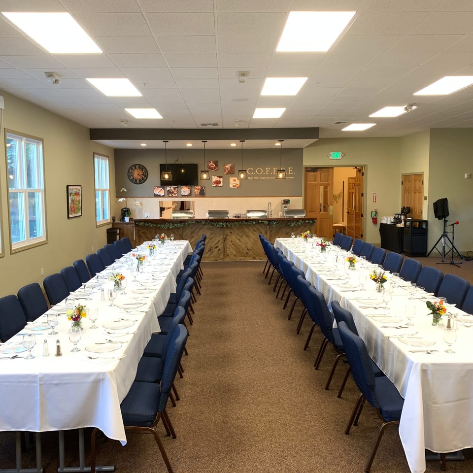 Two long tables set with white tablecloths and blue chairs in a spacious dining hall.