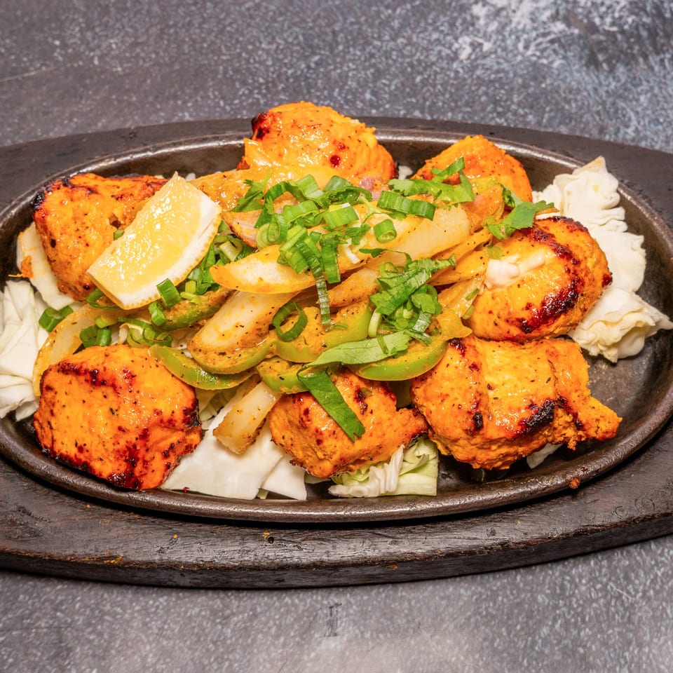 Indian chicken tikka with onions, peppers, and lemon on a sizzling platter.