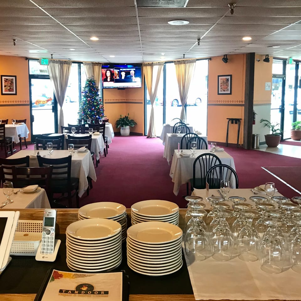 Interior of Tandoor Restaurant with set tables, red carpet, and a Christmas tree by the window.