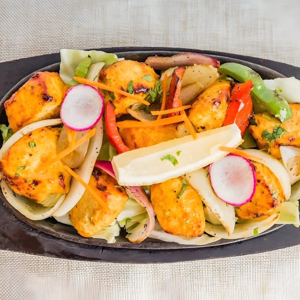 Indian chicken tikka sizzler with onions, bell peppers, radishes, and lemon on a hot plate.
