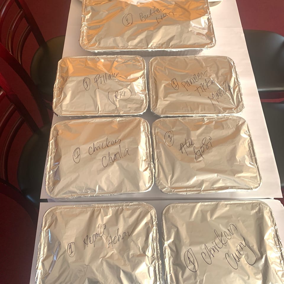 Several foil-covered Indian food containers, labeled with dishes like Butter Nan, Paneer Tikka, and Chicken Curry.