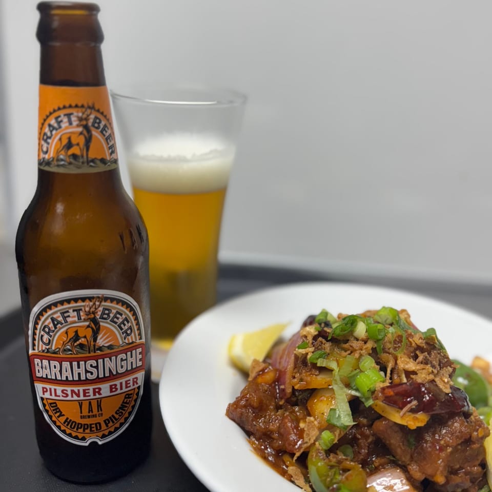 Barahsinghe Pilsner beer bottle and glass next to a plate of Indian chili chicken.